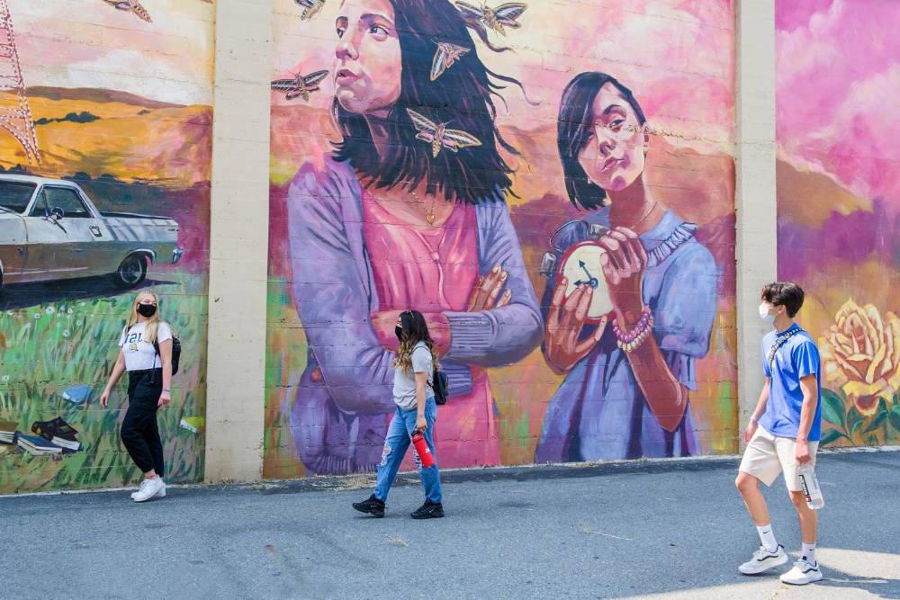 Students roaming downtown in front of a colorful mural.